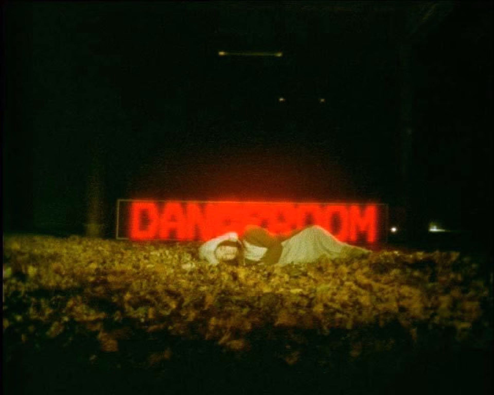 Donkere scène met persoon op bladeren onder felrood bord met tekst danger room, benadrukt waarschuwing - je bent hier mijn liefste