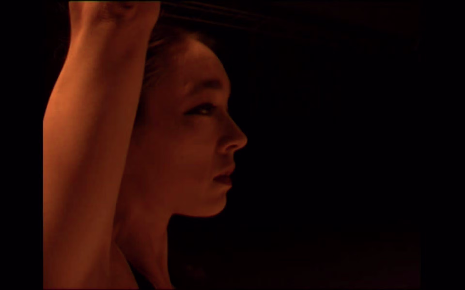 Side profile of a face and raised arm in low light capturing emotion under the heading DE TIJD