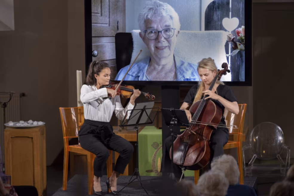 Live muziek met viool en cello, virtuele deelnemer op scherm, hybride evenement Stichting Be-wonder