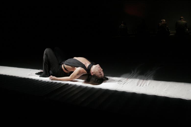 Dance Theater Film scène met expressieve danser in donkere setting, focus op lichaamshouding en emotie tijdens podiumvoorstelling